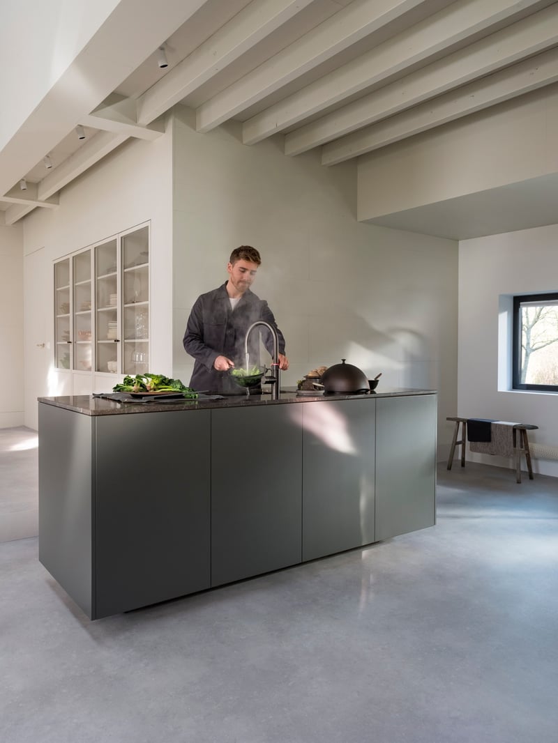 Quooker Flex Round in gunmetal boiling water tap — with AWO touch-free control, pouring 100 °C boiling water, rinsing leafy greens in a real customer kitchen. Genuine Quooker product supplied by Watertap.eu.