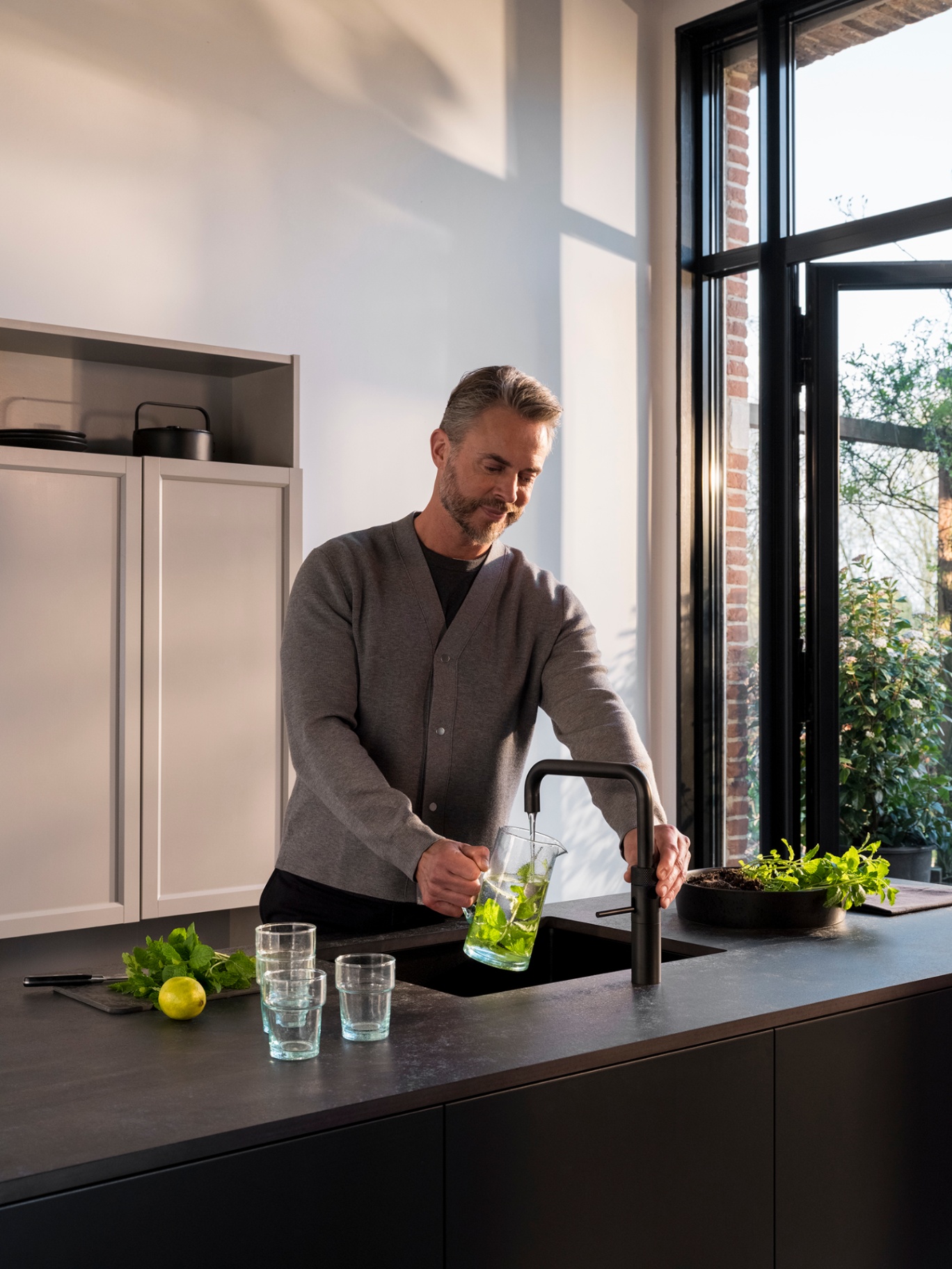 Quooker Fusion Square in black — filling a mint water carafe in a dark architectural kitchen, from Watertap.eu