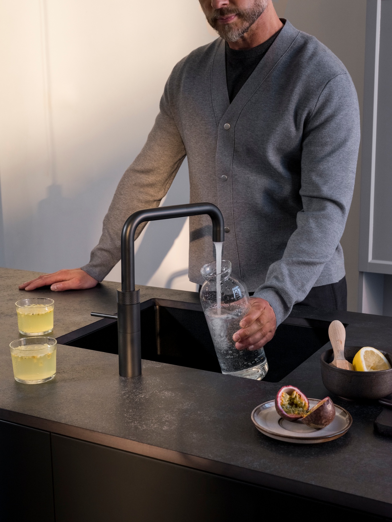 Close-up of a black Fusion Square Quooker filling a carafe with sparkling water beside citrus