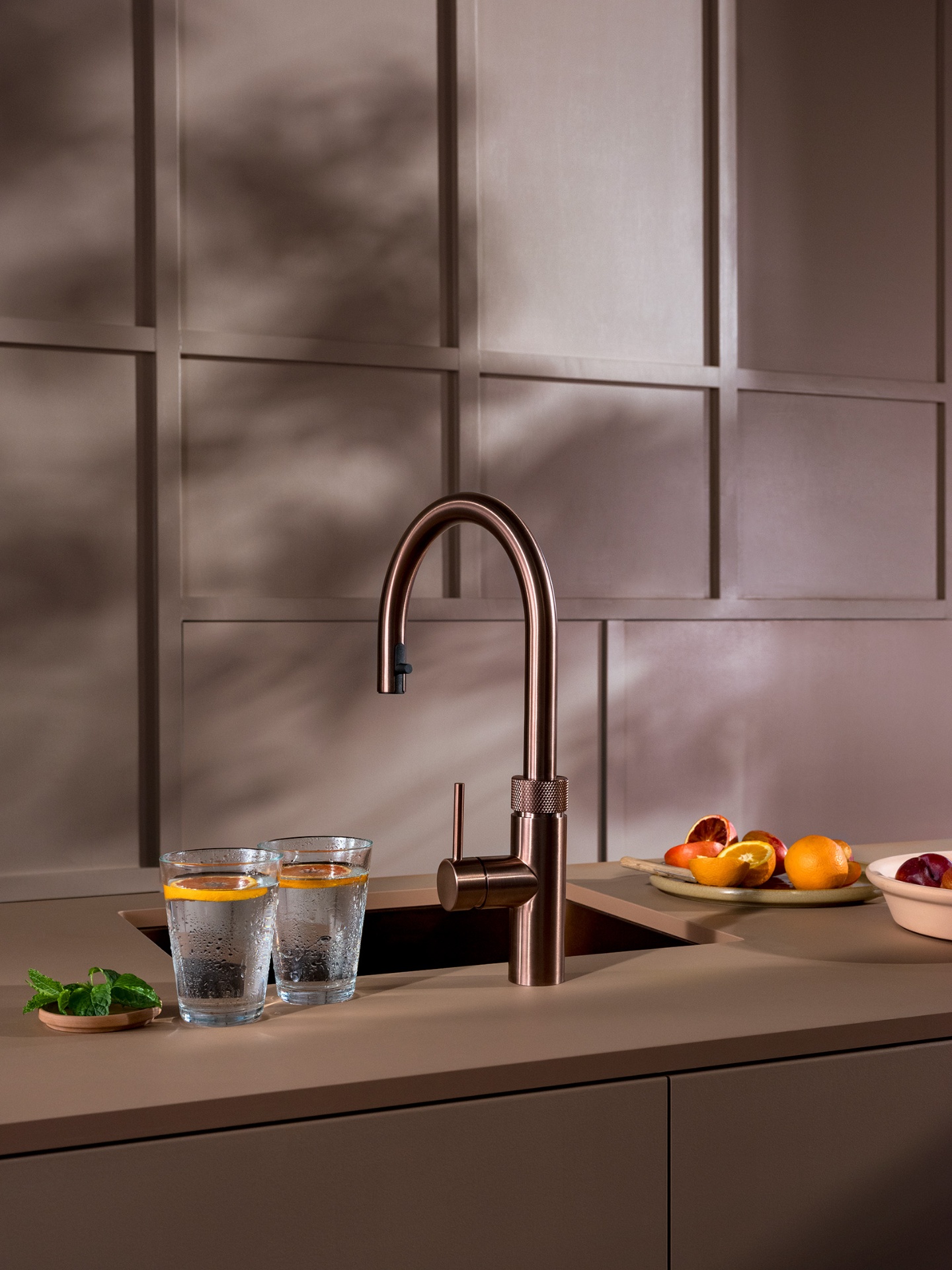 Still life of Flex Round rose copper Quooker with chilled orange water glasses in a taupe kitchen
