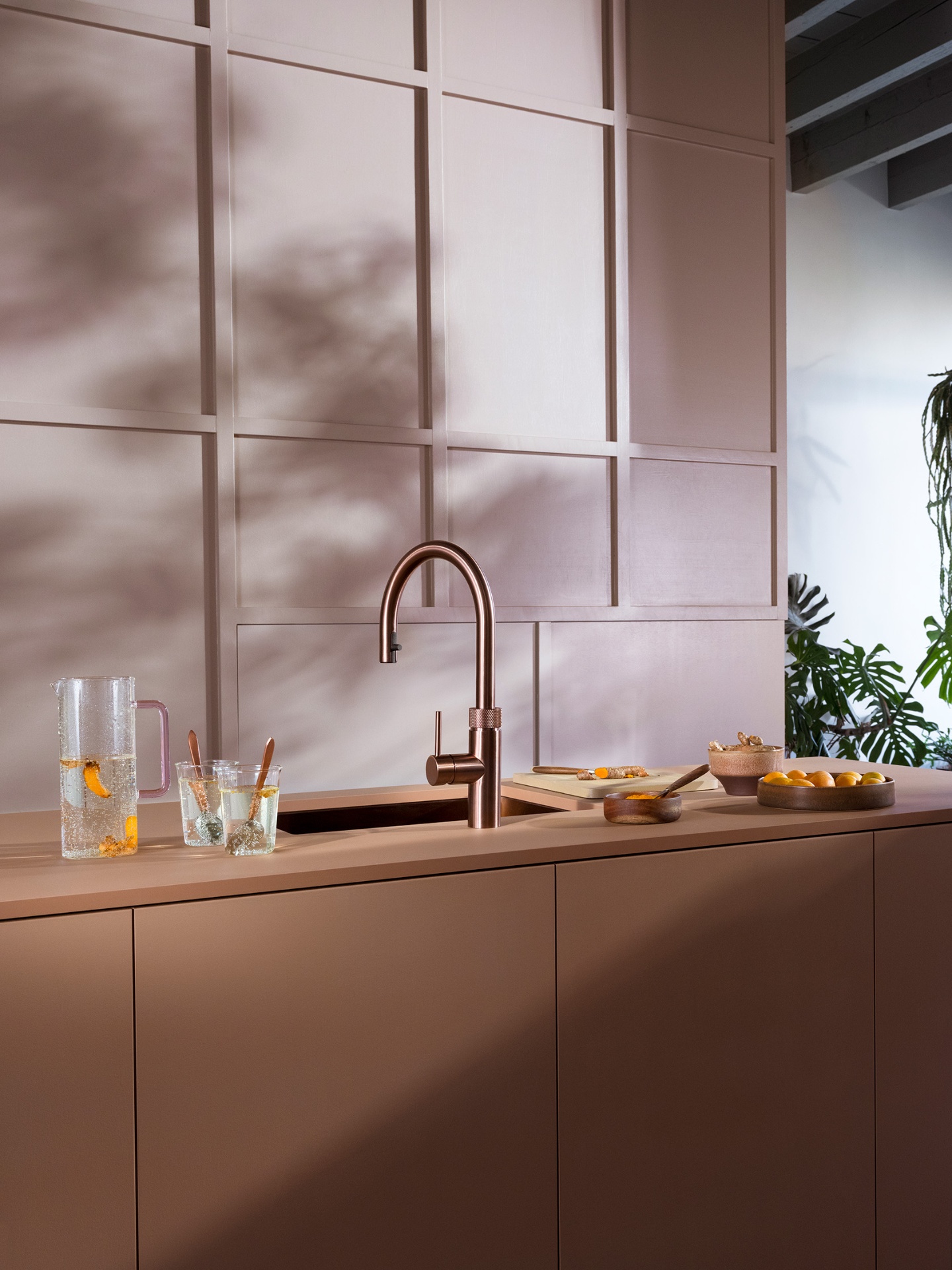 Editorial still of a Flex Round rose copper Quooker with orange-infused sparkling carafe on a blush panelled kitchen